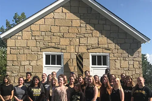 Students posing for photo in front of one-room schoolhouse at Emporia State
