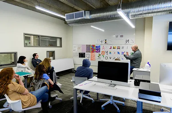 Students seated watching professor at white board demonstrating graphic design